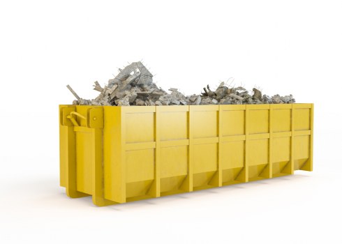 A large, rectangular skip with a bright yellow colour and sturdy metal construction, filled with broken concrete, rubble, and assorted debris. The skip is positioned on a clean, white surface, with its open top revealing the irregular, jagged mixture of concrete chunks, stones, and fragments of construction materials inside. The background is plain and uncluttered, emphasizing the skip and its contents. The surface texture of the concrete varies from smooth broken surfaces to rough, jagged edges, highlighting the demolition waste typically handled by commercial waste services in Balham. The skip’s side panels are smooth with visible panels and hinges, while the debris is piled unevenly, leaning slightly towards the front. This scene illustrates waste collection and disposal in a professional context, supporting services such as those offered by Commercial Waste Balham, which specialises in rubbish removal from construction, renovation, or commercial sites in the local area.